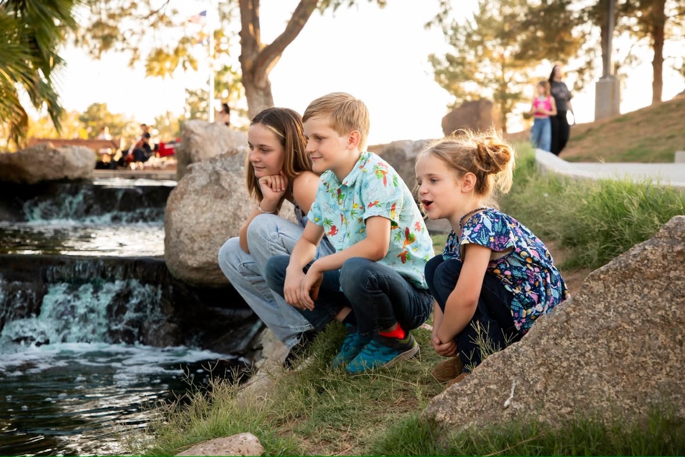 Olivia crouched by a park stream with her younger brother and sister
